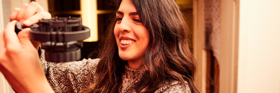 A young woman with long hair smiling as she adjusts a microphone